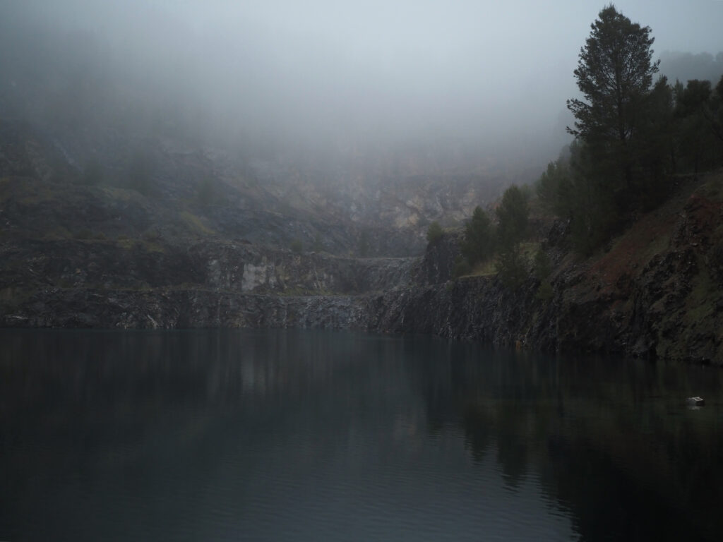 Crystal Quarry (Highbury) at dawn on a rainy/foggy morning. The stone and trees are reflected in the water but part of the quarry is not visible due to mist.